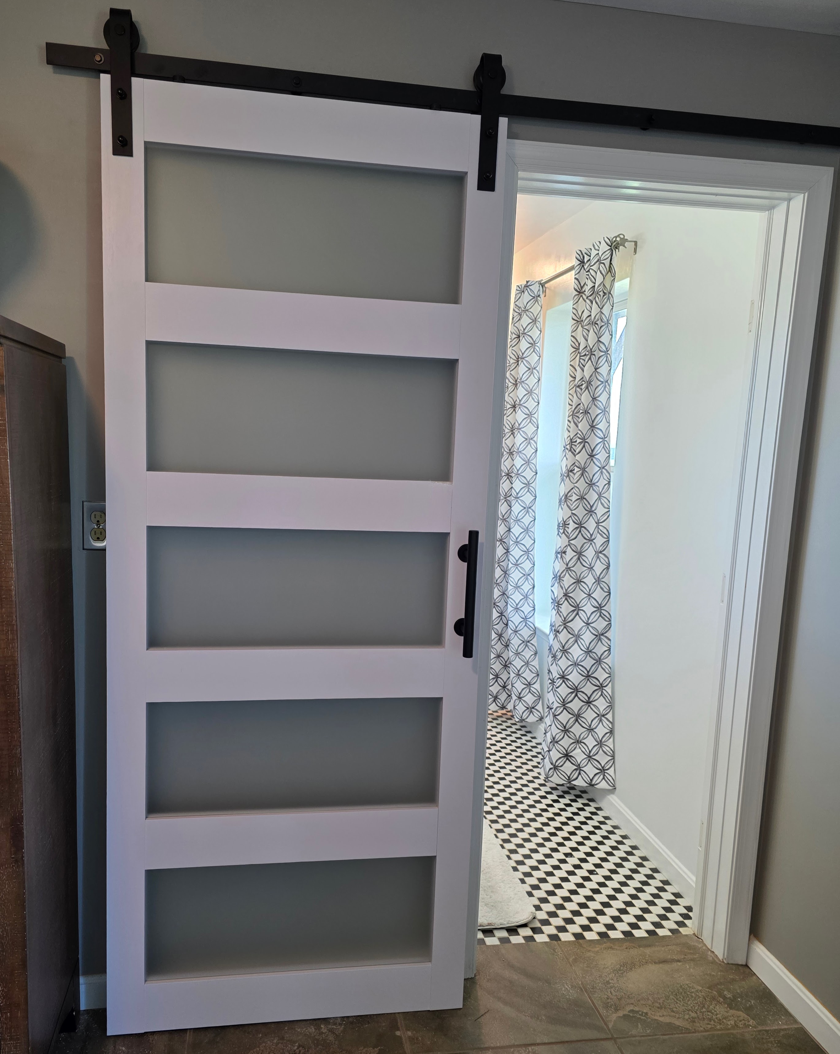 White frosted-glass barn door half open into a checkered bathroom
